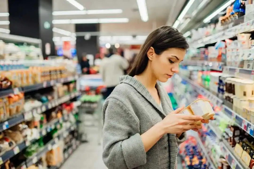 Woman shopping a dairy product in the supermarket grocery store.Reading ingredients,declaration or expiration date before buying it.Nutritional value of the food.Lactose intolerance information; Shutterstock ID 1694722042