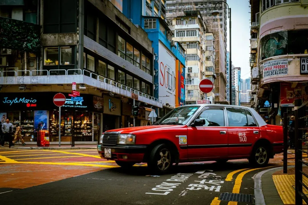 a red car driving down a street next to tall buildings