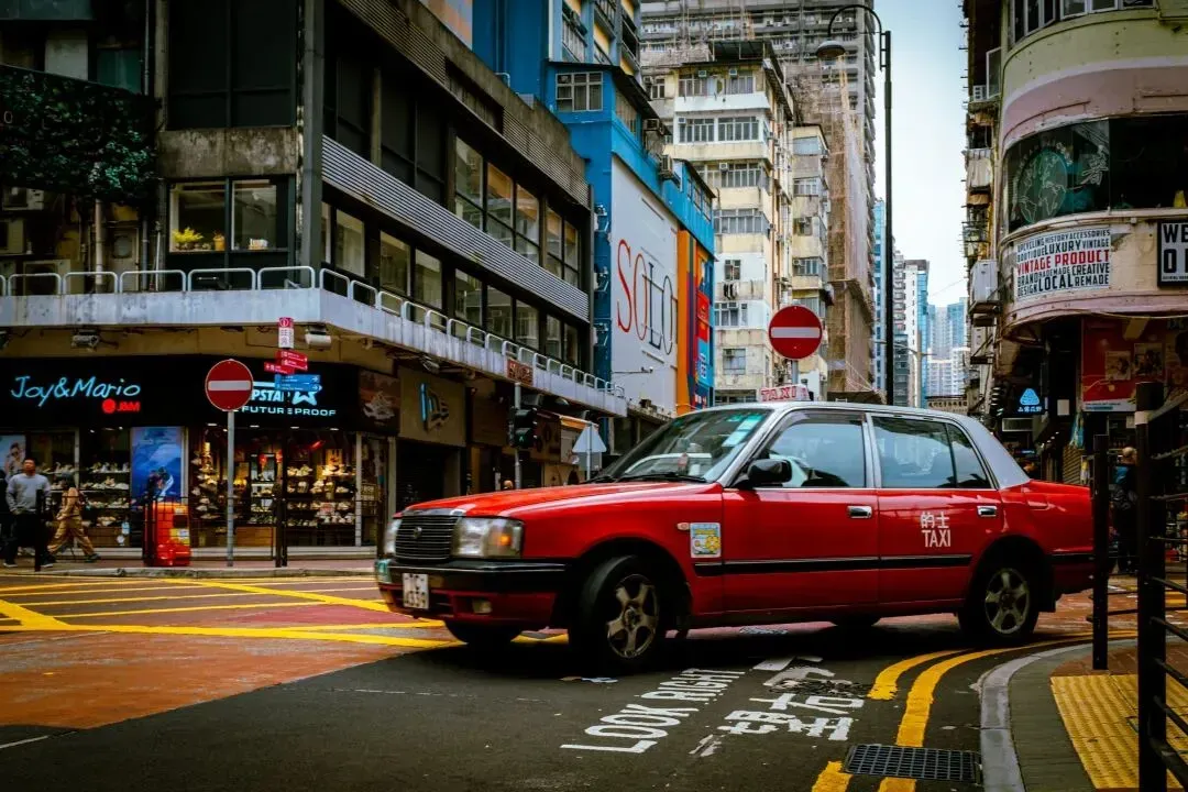 a red car driving down a street next to tall buildings