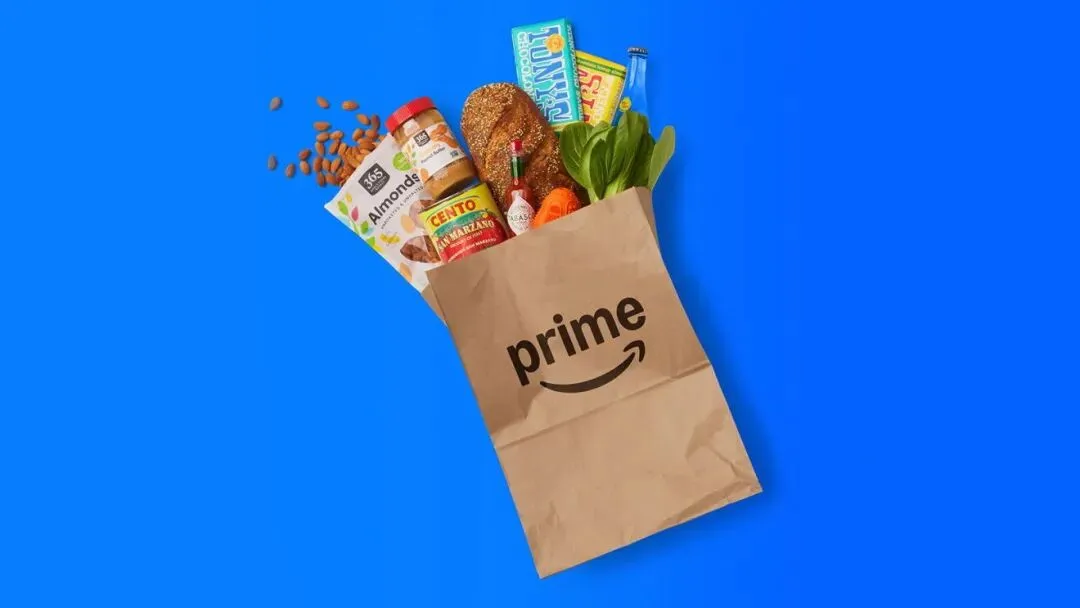 Amazon Prime grocery bag filled with fresh produce, bread, and pantry items on blue background
