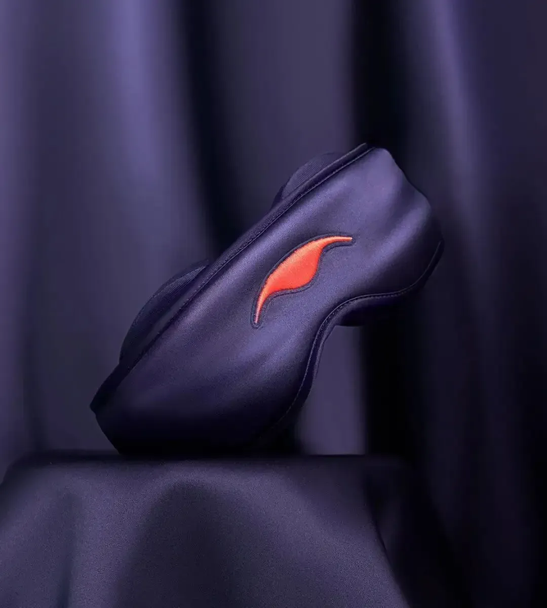 A purple silk sleep mask balancing elegantly on a pedestal draped in matching lustrous purple fabric.