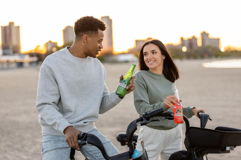 穿白色毛衣的男人拿着绿色瓶子，旁边是穿白色毛衣的女人骑自行车
