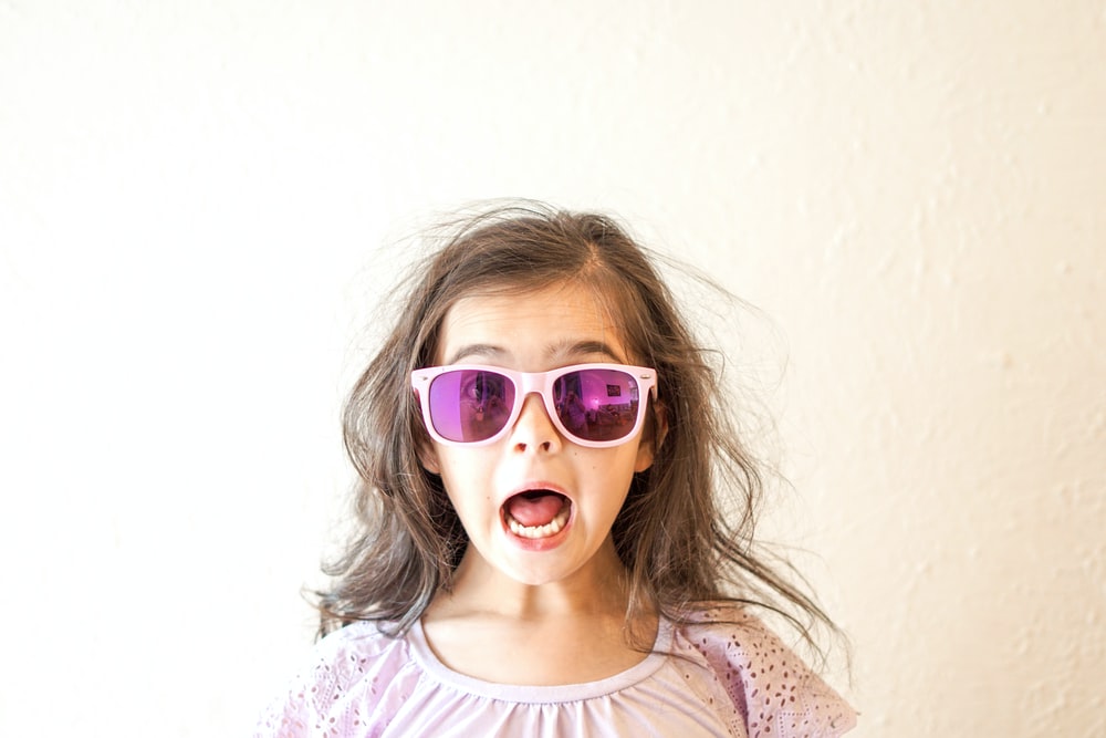 身穿白色和紫色花卉圆领衬衫、戴着蓝色框太阳镜的女孩