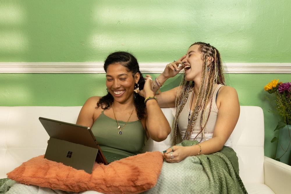 two women sitting on a couch talking on their cell phones